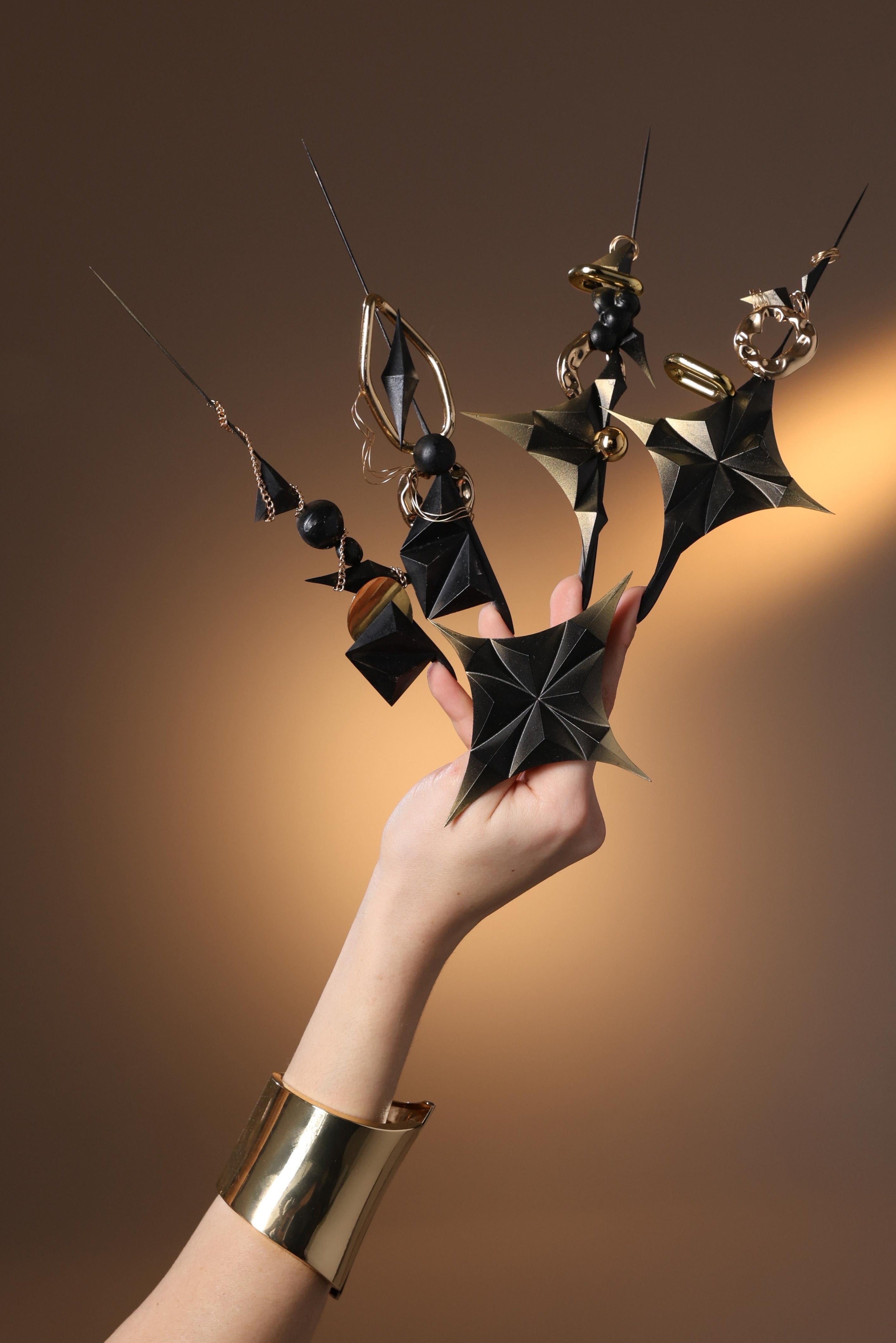Hand holding a decorative black and gold object against a warm brown background